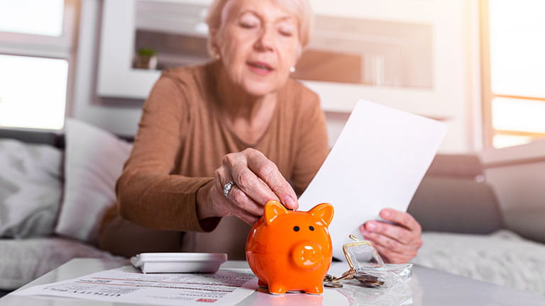Woman putting money into piggy bank while holding retirement papers